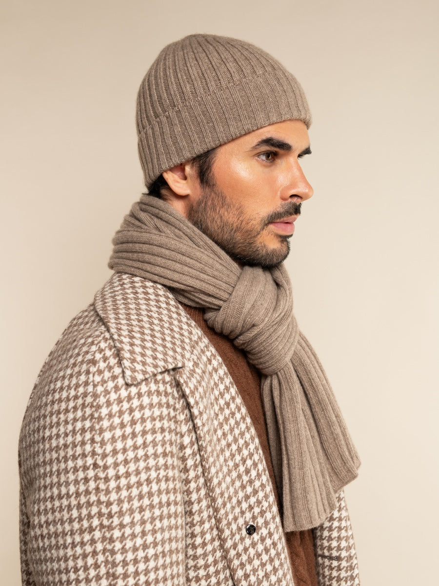 Man wearing a patterned coat, beanie, and scarf against a beige background