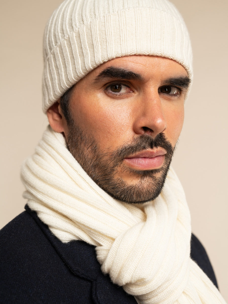 Man wearing an ivory cashmere knit beanie and scarf against a beige background