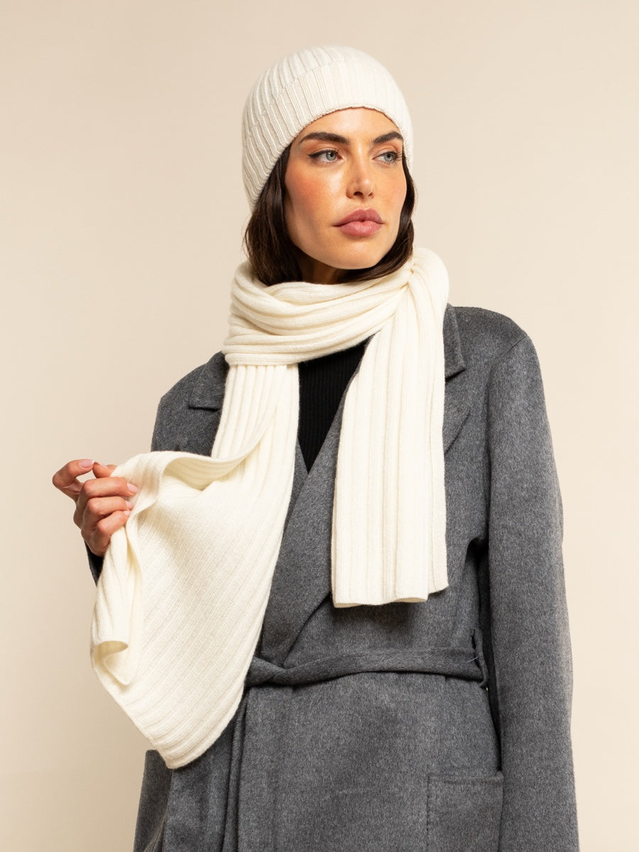 Woman wearing an ivory cashmere knit hat and scarf against a beige background