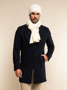 Man wearing a navy coat, ivory scarf, and knit hat against a beige background