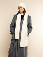 Person wearing a gray coat, ivory scarf, and beanie on a beige background