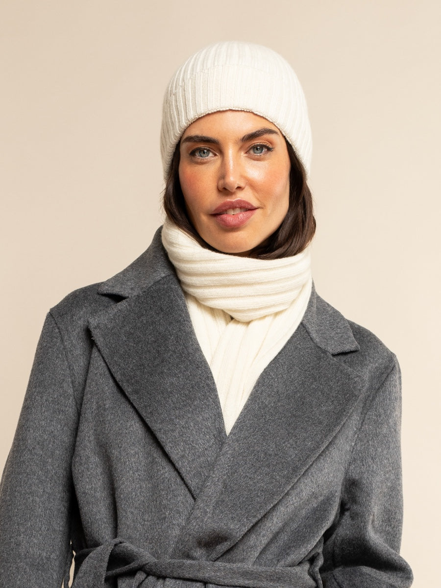 Woman wearing an ivory cashmere knit beanie and scarf with a gray coat on a beige background