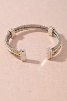 A silver-toned cable cuff bracelet with polished rectangular silver end pieces and small gold-toned accents, photographed on a soft pink background.