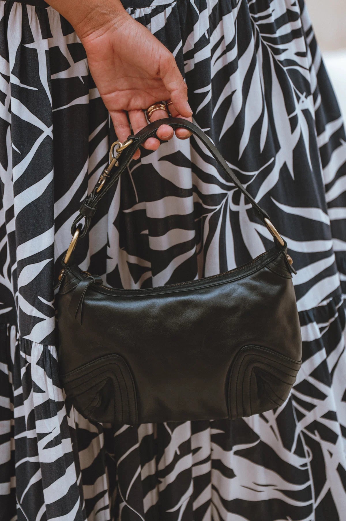 Person holding a black leather handbag with a patterned dress in the background