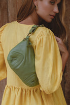 Woman wearing a yellow dress with a green bag over her shoulder against a wooden background