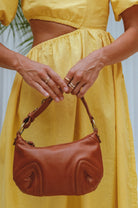 Person wearing a yellow dress holding a camel handbag with a blurred background