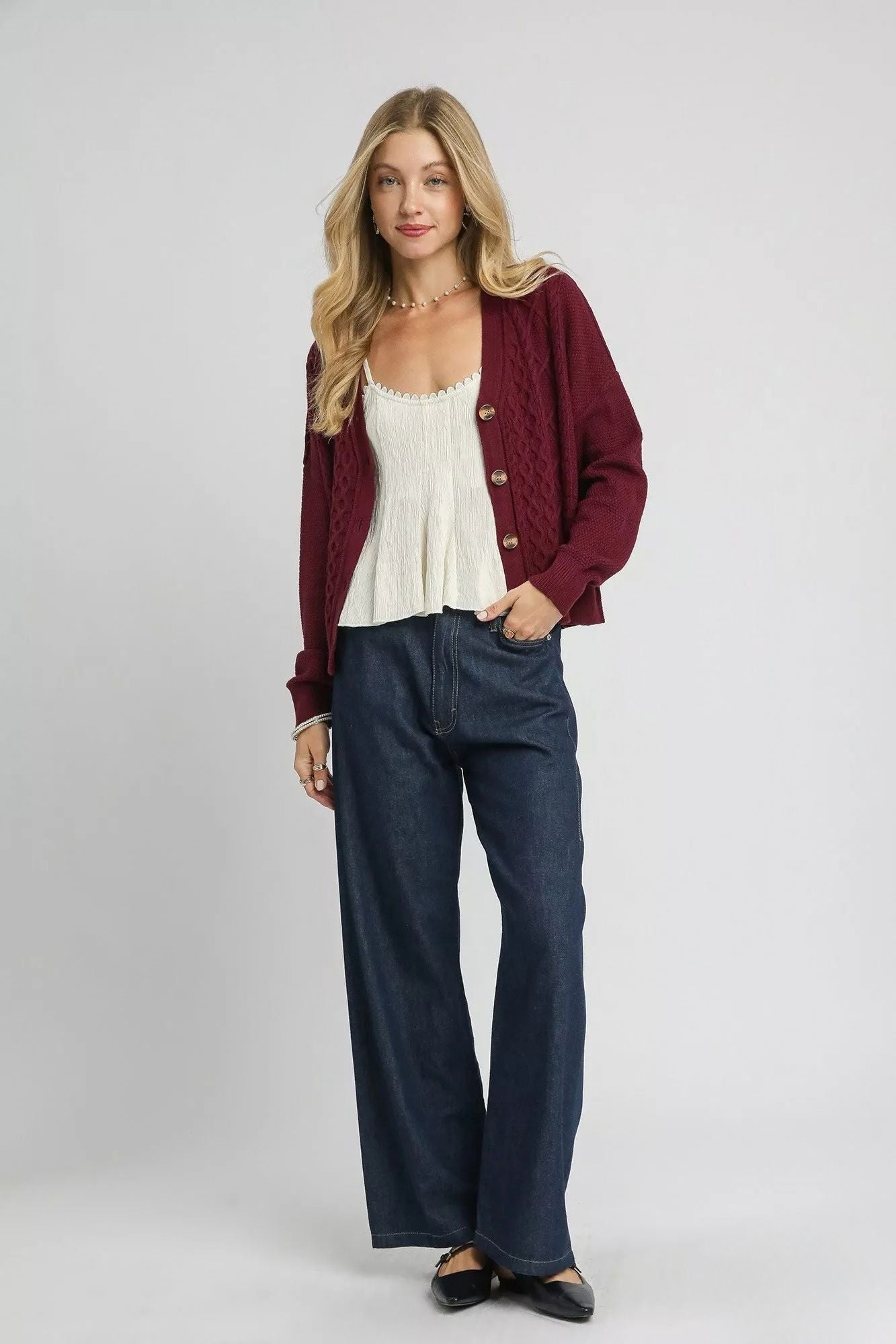 Bordeaux burgundy cable knit cardigan styled open with an ivory top and dark wide leg jeans.