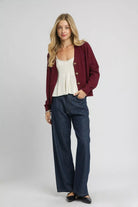 Bordeaux burgundy cable knit cardigan styled open with an ivory top and dark wide leg jeans.