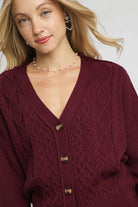 Close up of Bordeaux burgundy cable knit cardigan showing mixed cable patterns, V neckline and tortoise style buttons.