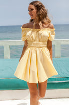 Woman in a yellow off-the-shoulder cotton mini dress standing by the ocean, front view