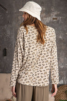 Back view of a beige leopard print oversized knit top with dolman sleeves and relaxed fit, styled with khaki jogger pants and bucket hat.

