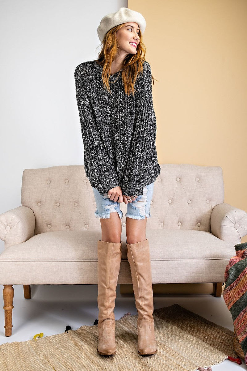 Model styled in a marled ribbed sweater, distressed denim shorts, and tall tan boots.
