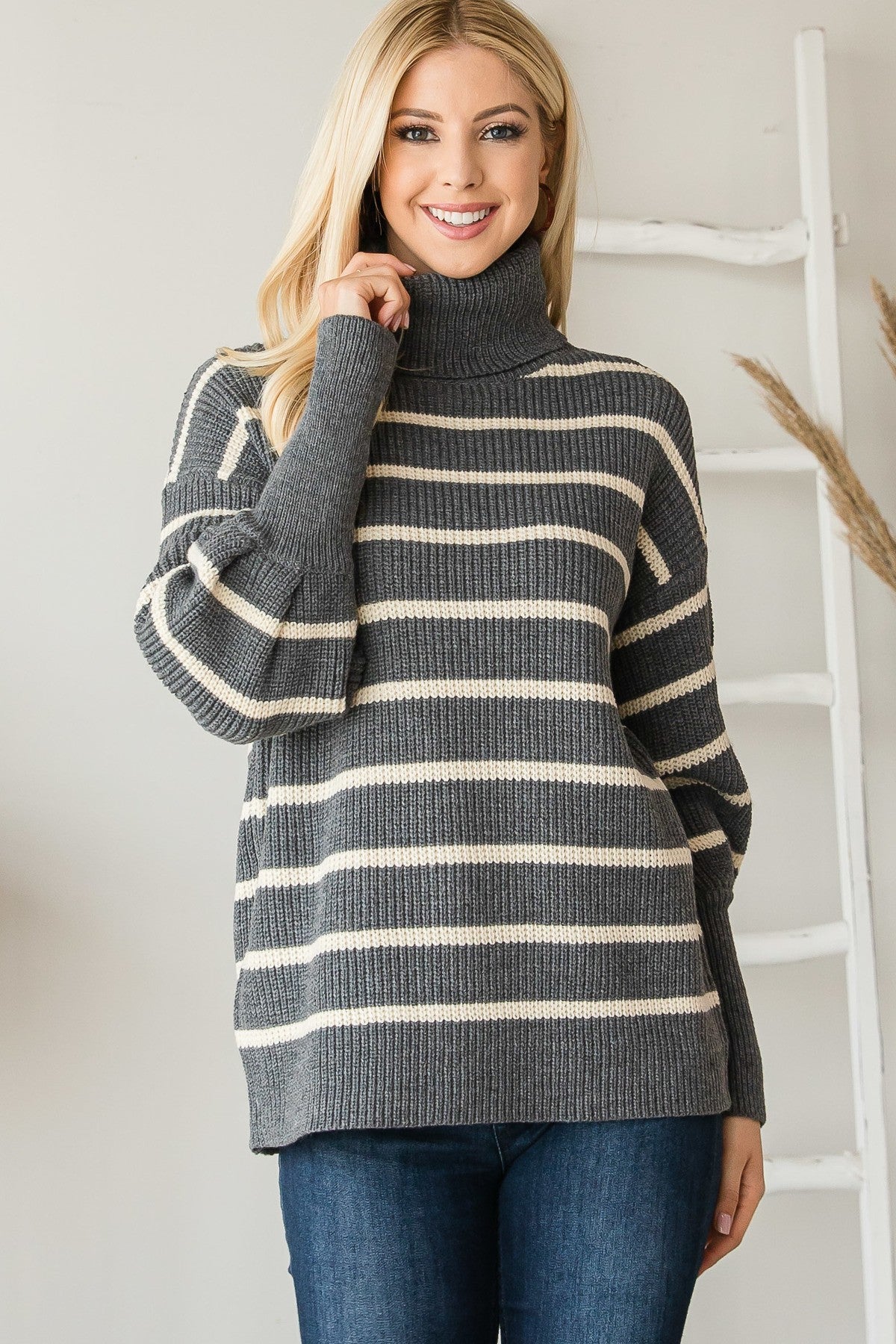 Grey and cream striped ribbed turtleneck sweater worn by a blonde model facing forward.