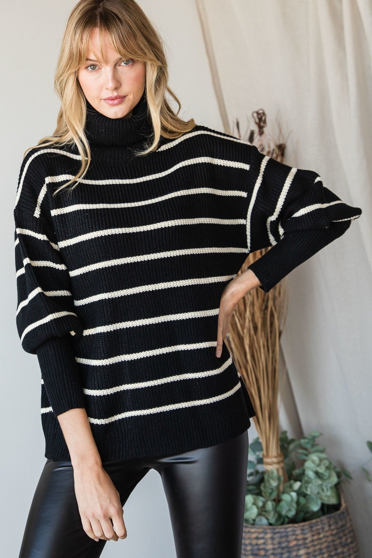 Model wearing a black and ivory striped oversized turtleneck sweater with long sleeves, paired with black faux-leather leggings.