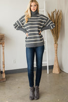 Full-length view of model wearing a grey and cream striped turtleneck sweater styled with dark jeans and grey ankle boots.
