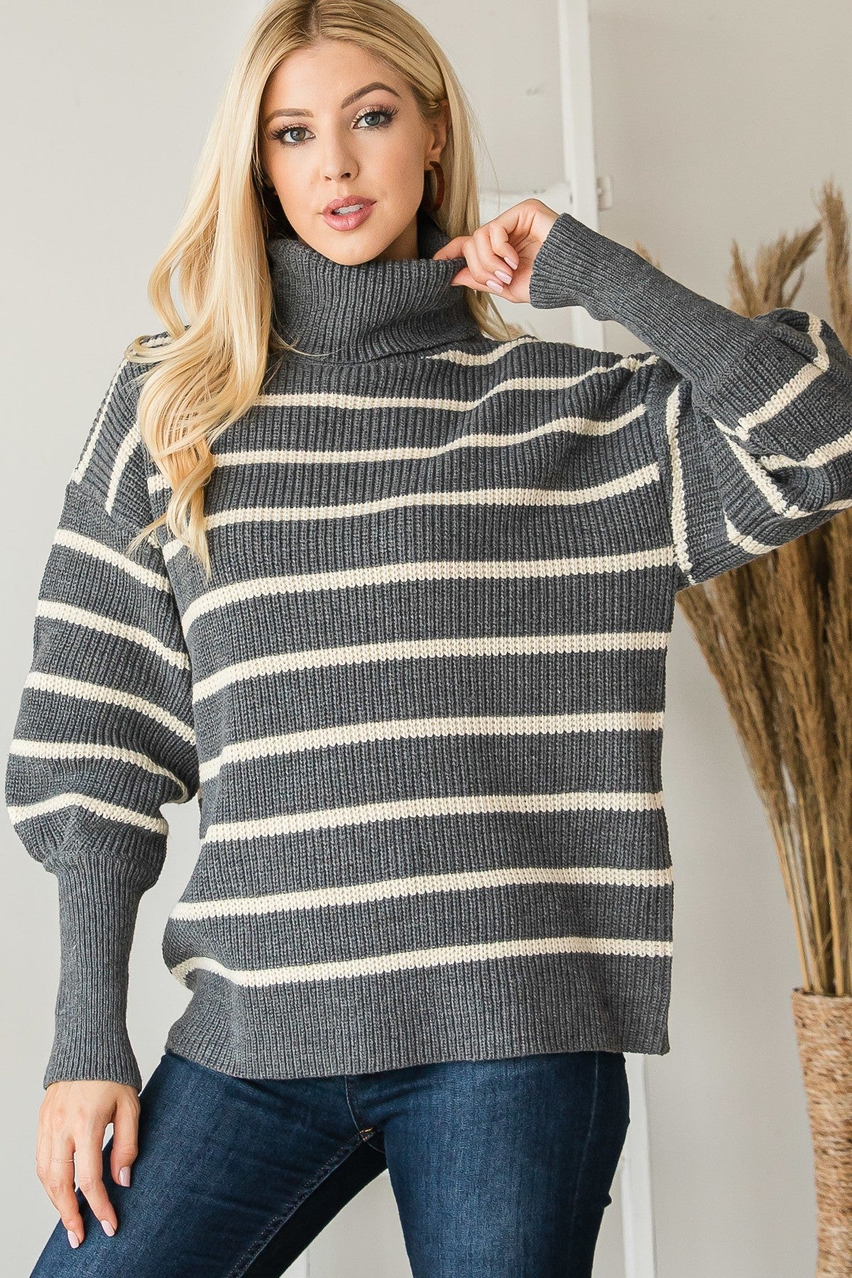 Model adjusting the turtleneck on a grey and cream striped ribbed sweater, showing the relaxed fit.