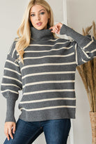 Model adjusting the turtleneck on a grey and cream striped ribbed sweater, showing the relaxed fit.