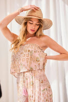 Woman wearing a blush bohemian strapless jumpsuit with flounce overlay bodice
