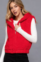 Woman wearing a red hooded plush zip vest layered over a white ribbed long-sleeve top.