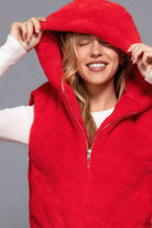 Close-up of a woman smiling with the hood of a red plush vest pulled over her head, zipper partially closed.