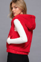 Back view of a woman wearing a bright red plush hooded vest over a white ribbed top, showing the oversized hood and smooth texture.