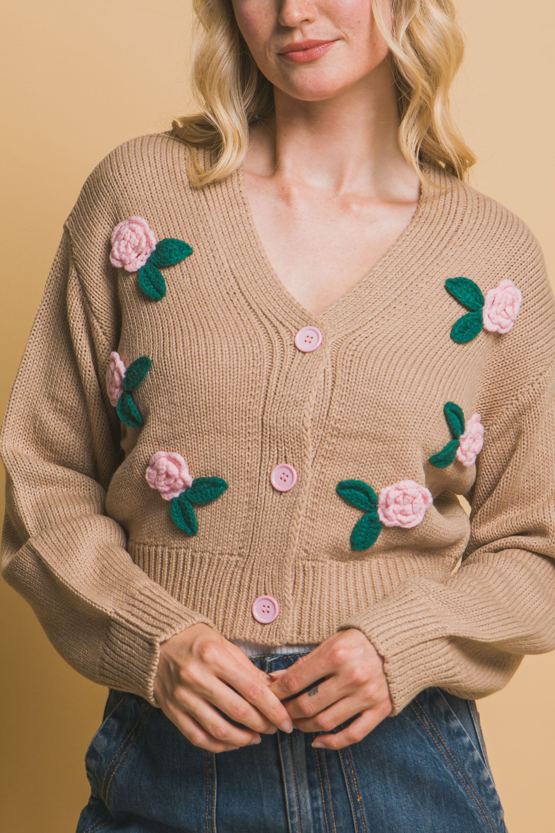 Close-up of open buttoned khaki cropped cardigan with floral appliqués