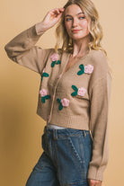 Side view of a khaki cropped cardigan with floral appliqué details and pink buttons, styled with denim cargo pants.