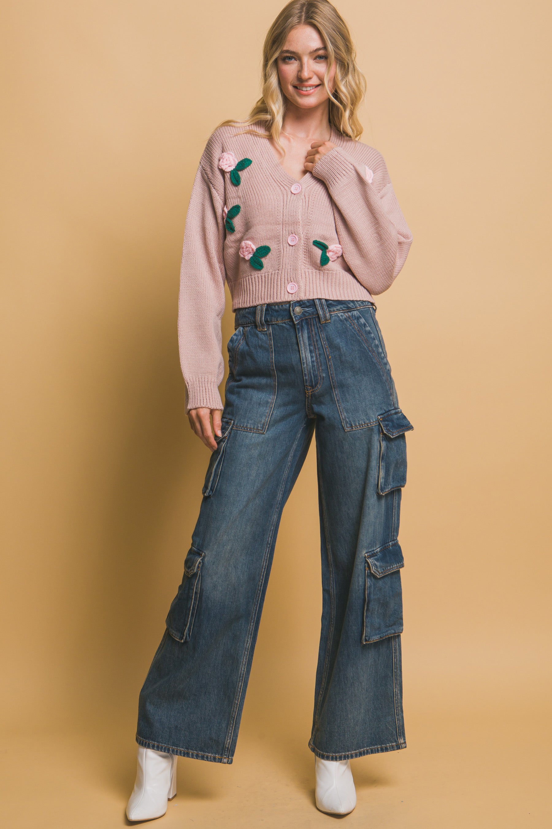 Full body view of model in dusty pink rose garden cropped cardigan paired with cargo-style jeans and white boots.