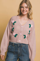 Model wearing dusty pink cropped cardigan with 3D floral appliqué, pink buttons, and wide-leg jeans.