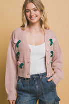Close-up of dusty pink floral button-up cardigan with pink rose appliqué and ribbed hem.