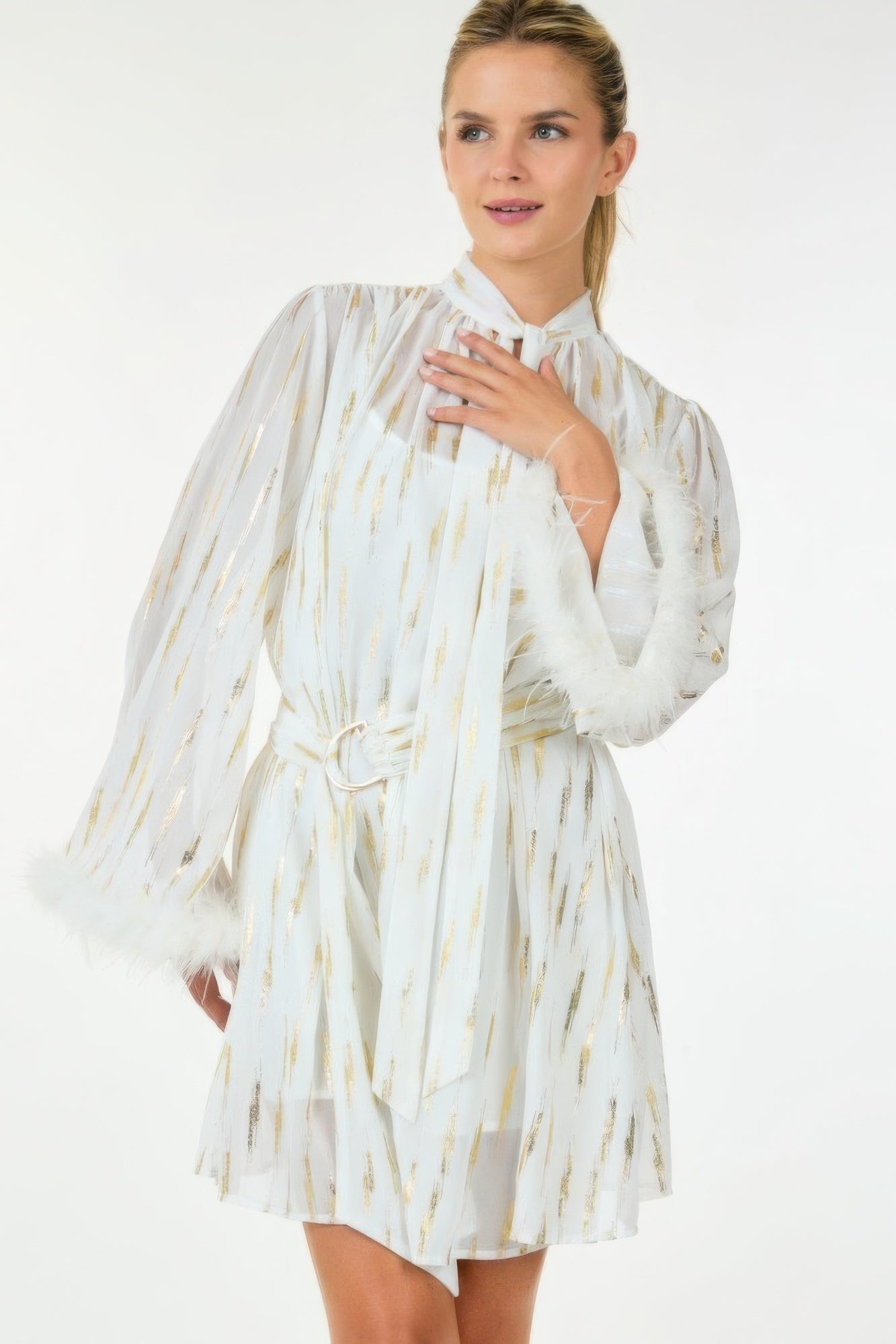 White and gold metallic mini dress with feather cuffs shown from the front as model poses with hand near neckline