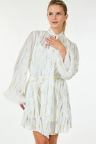 White and gold metallic mini dress with feather cuffs shown from the front as model poses with hand near neckline