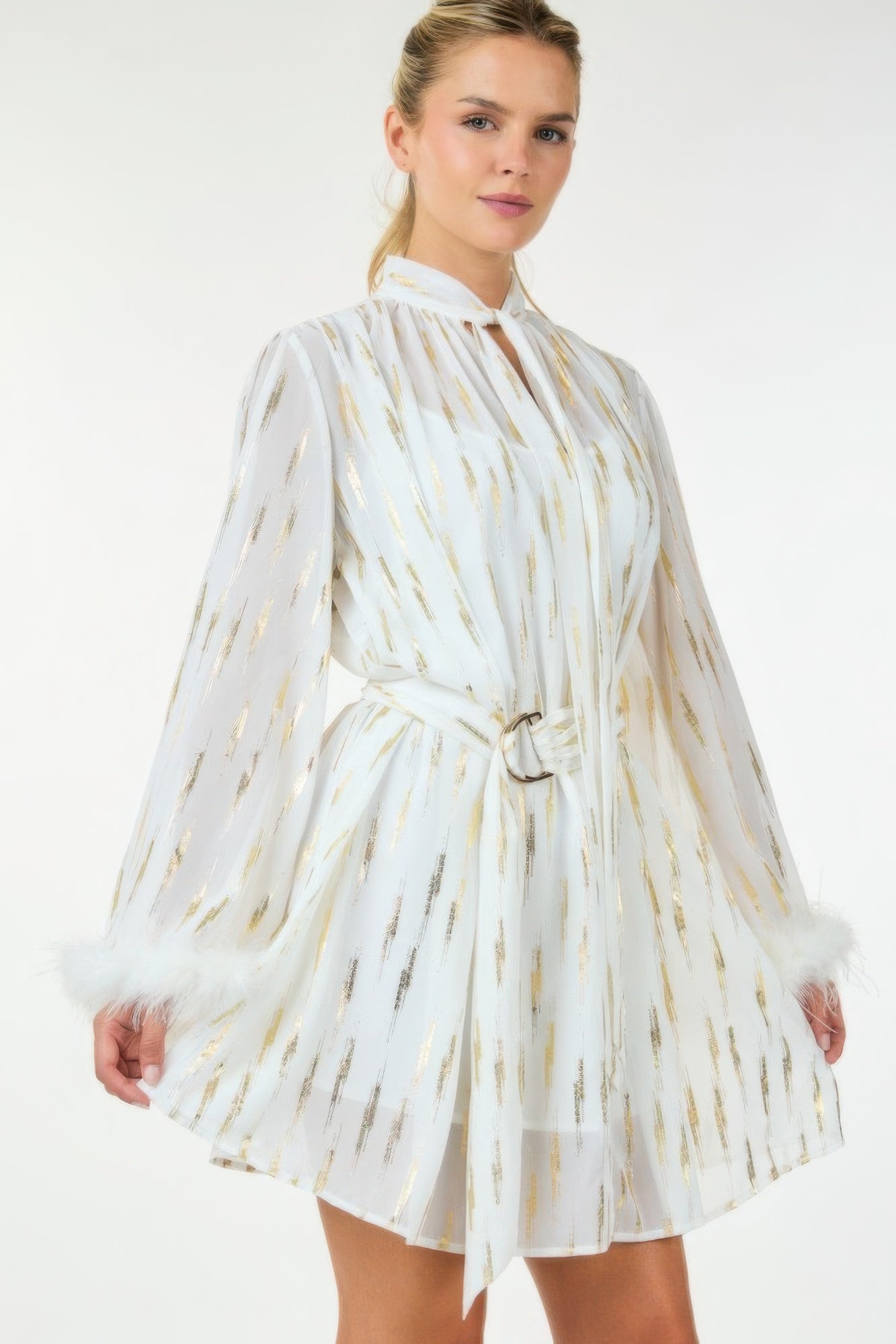 Model wearing white and gold feather-trim mini dress with tie neck and belted waist, front view.