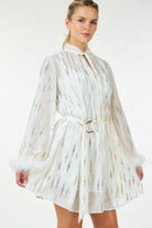 Model wearing white and gold feather-trim mini dress with tie neck and belted waist, front view.