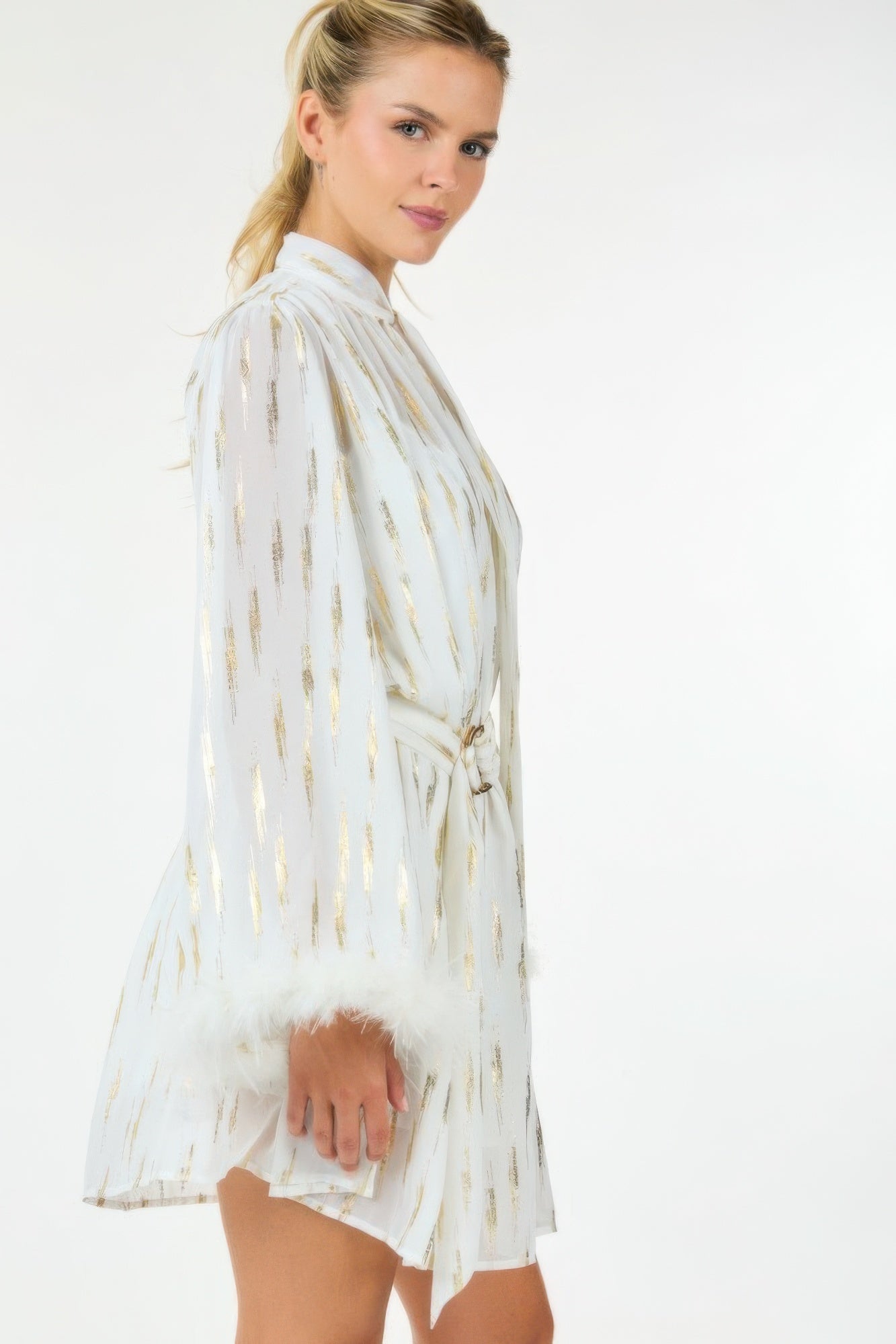 Side view of white metallic mini dress with feather cuffs and flowing sleeves.