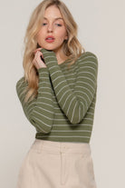 Close-up of the olive ribbed long sleeve top with white stripes, styled with beige high-waisted trousers.
