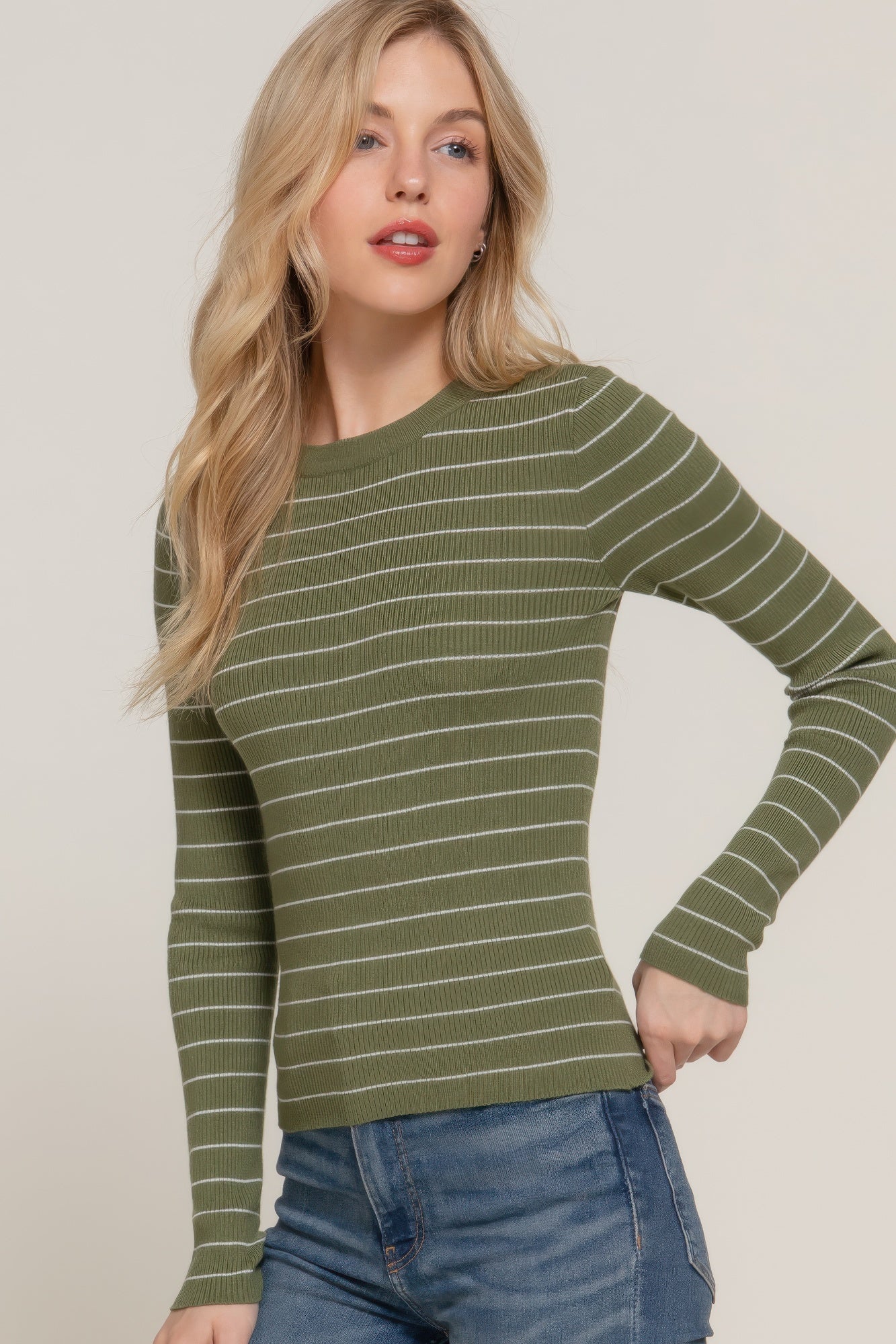 Model posing in an olive striped ribbed knit top and blue jeans, showing the fitted silhouette from mid-thigh up.