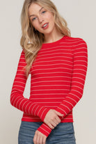 Model wearing a red long sleeve ribbed knit top with white horizontal stripes, shown from the waist up with one sleeve gently pulled.
