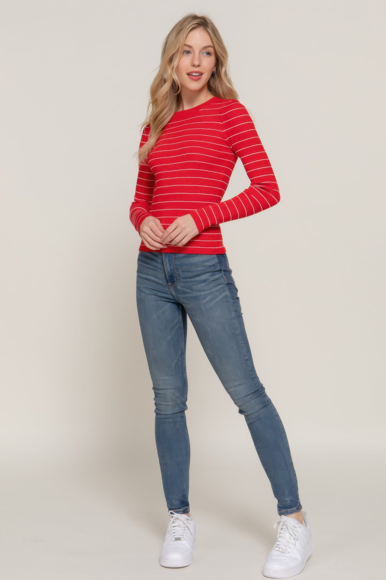 Full-body view of model in a red and white striped ribbed top paired with light wash skinny jeans and white sneakers.
