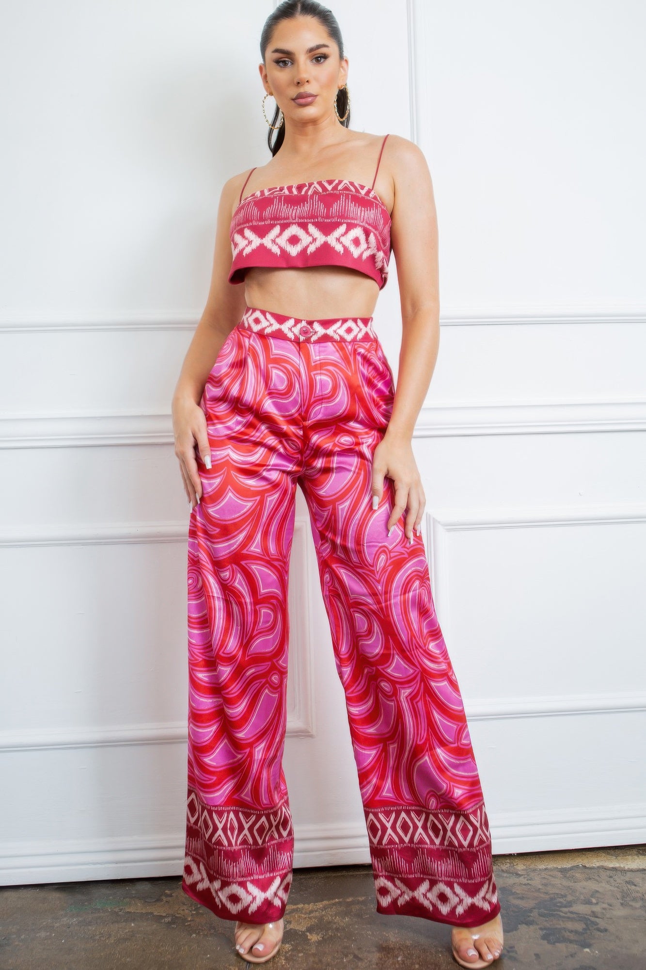 Model wearing a pink satin two piece set featuring a cropped camisole top and wide leg printed pants.
