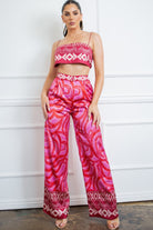 Model wearing a pink satin two piece set featuring a cropped camisole top and wide leg printed pants.
