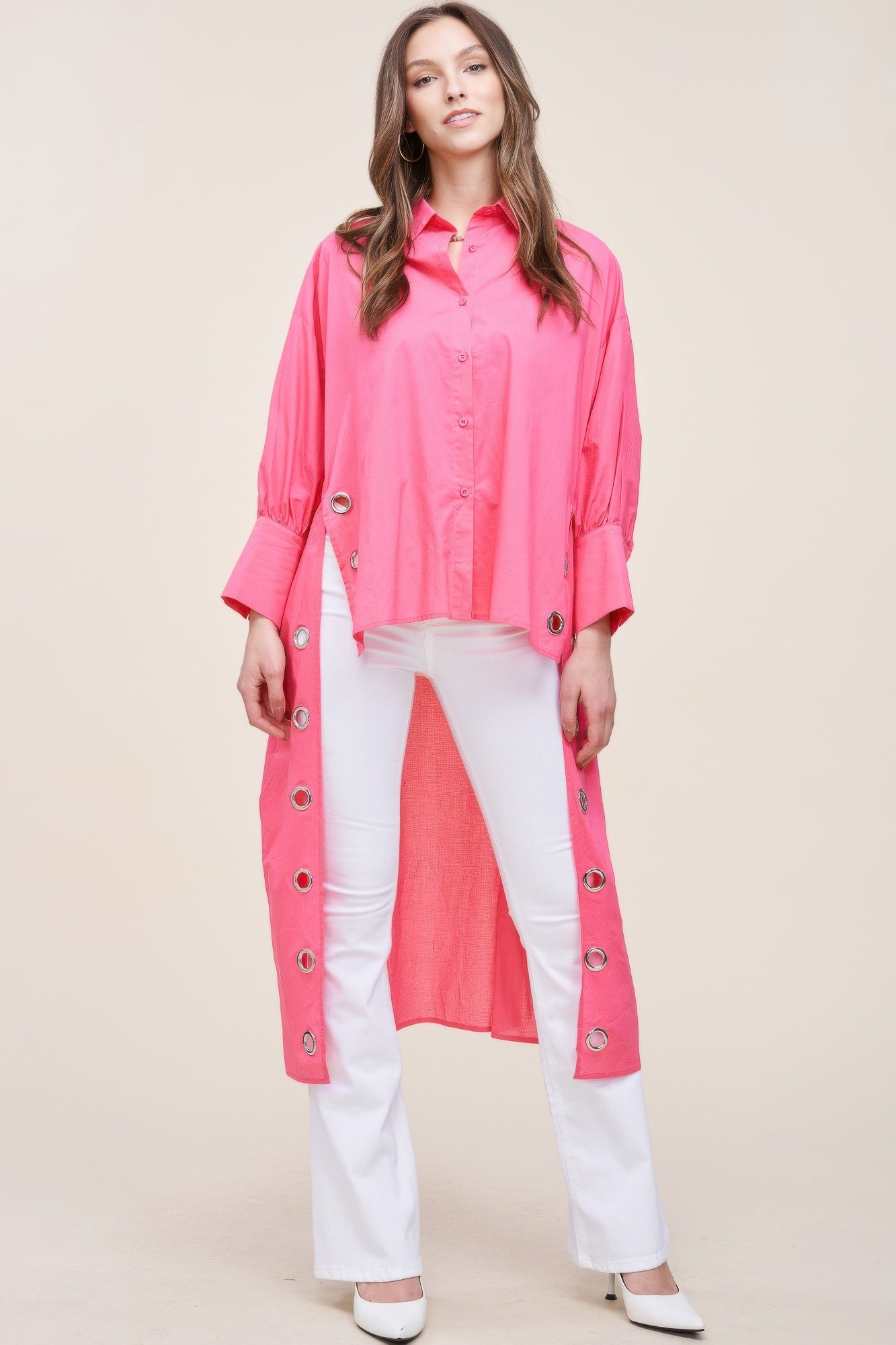 Model wearing an oversized electric pink cotton duster shirt with silver grommet detailing and longline back hem.