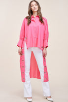 Model wearing an oversized electric pink cotton duster shirt with silver grommet detailing and longline back hem.