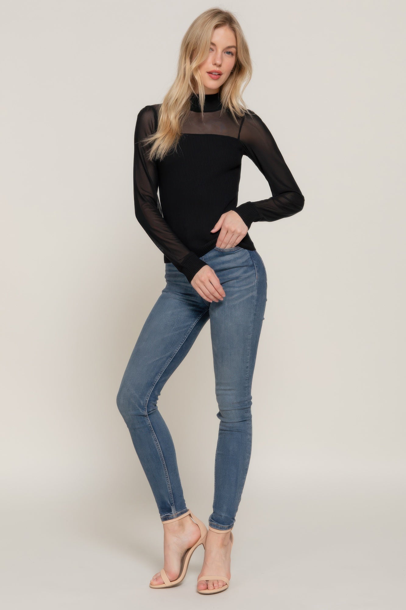 Woman wearing a black long-sleeve top and blue jeans on a plain background