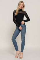 Woman wearing a black long-sleeve top and blue jeans on a plain background
