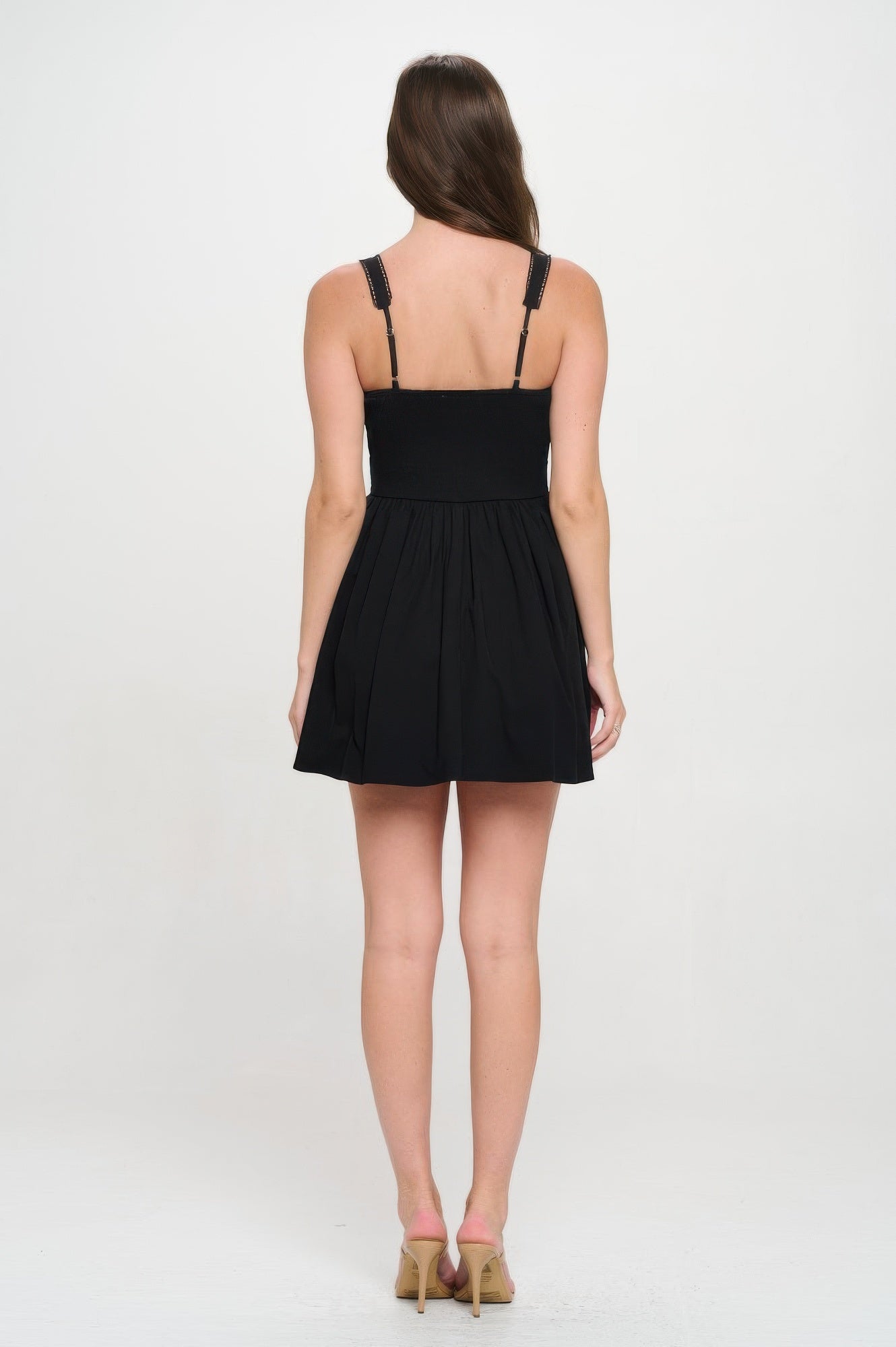Back view of black mini dress with smocked panel and flared pleated skirt.