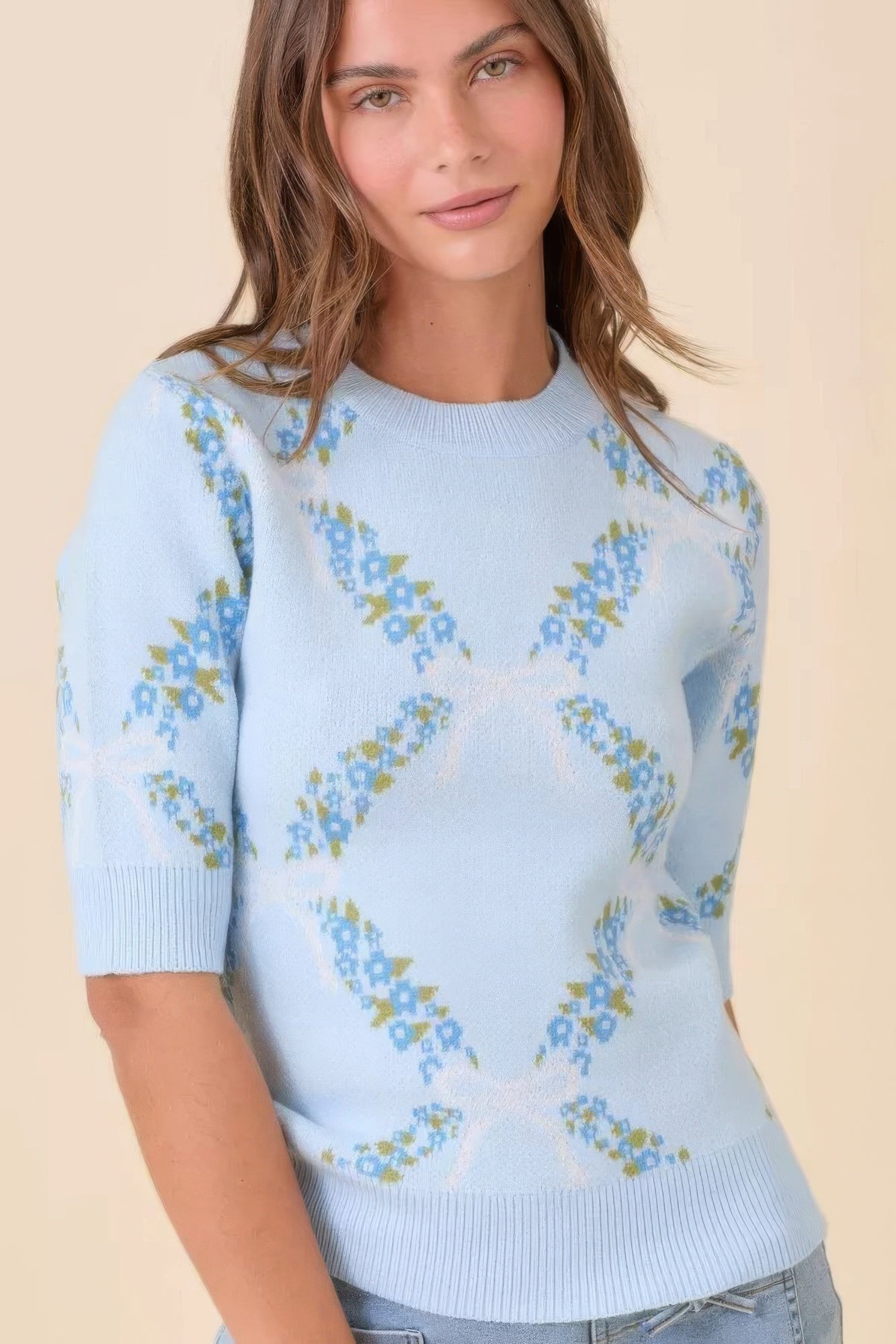Model wearing light blue floral-pattern short sleeve knit sweater, front view.
