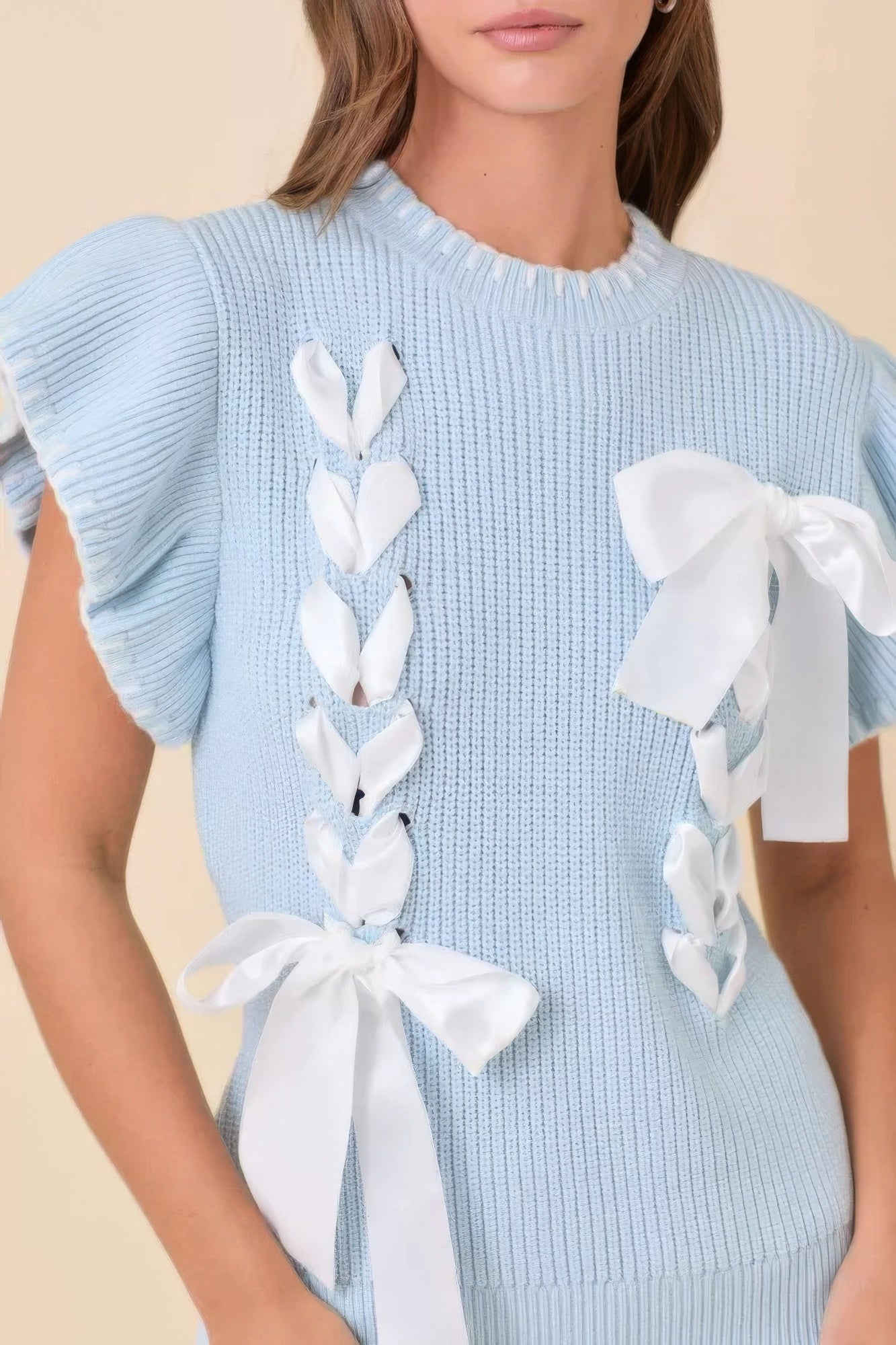 Close-up of baby-blue knit sweater showing satin ribbon lacing and ruffled sleeves.