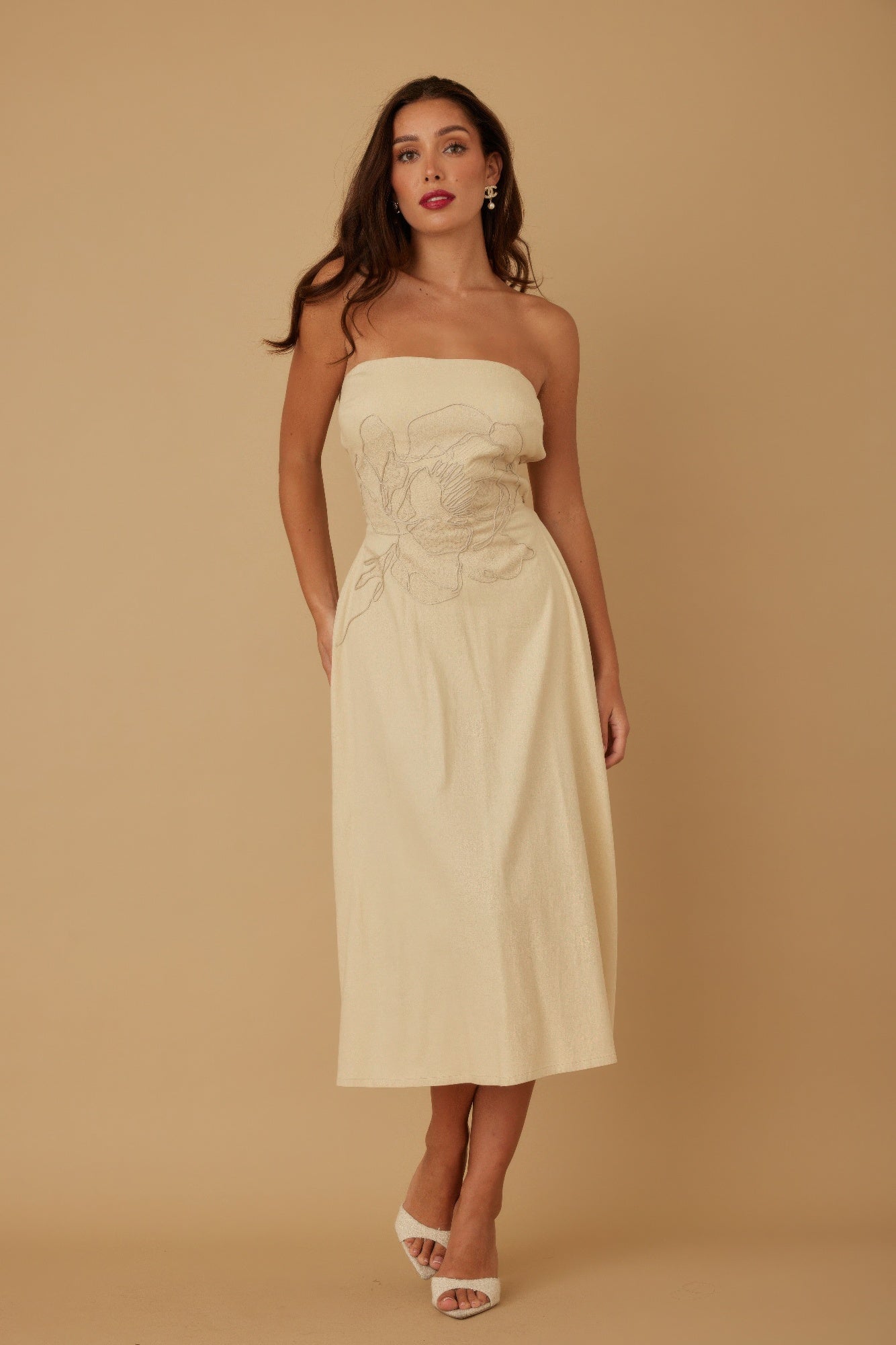 Front view of model wearing beige strapless embroidered midi dress with white heels
