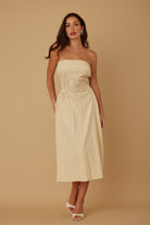Front view of model wearing beige strapless embroidered midi dress with white heels
